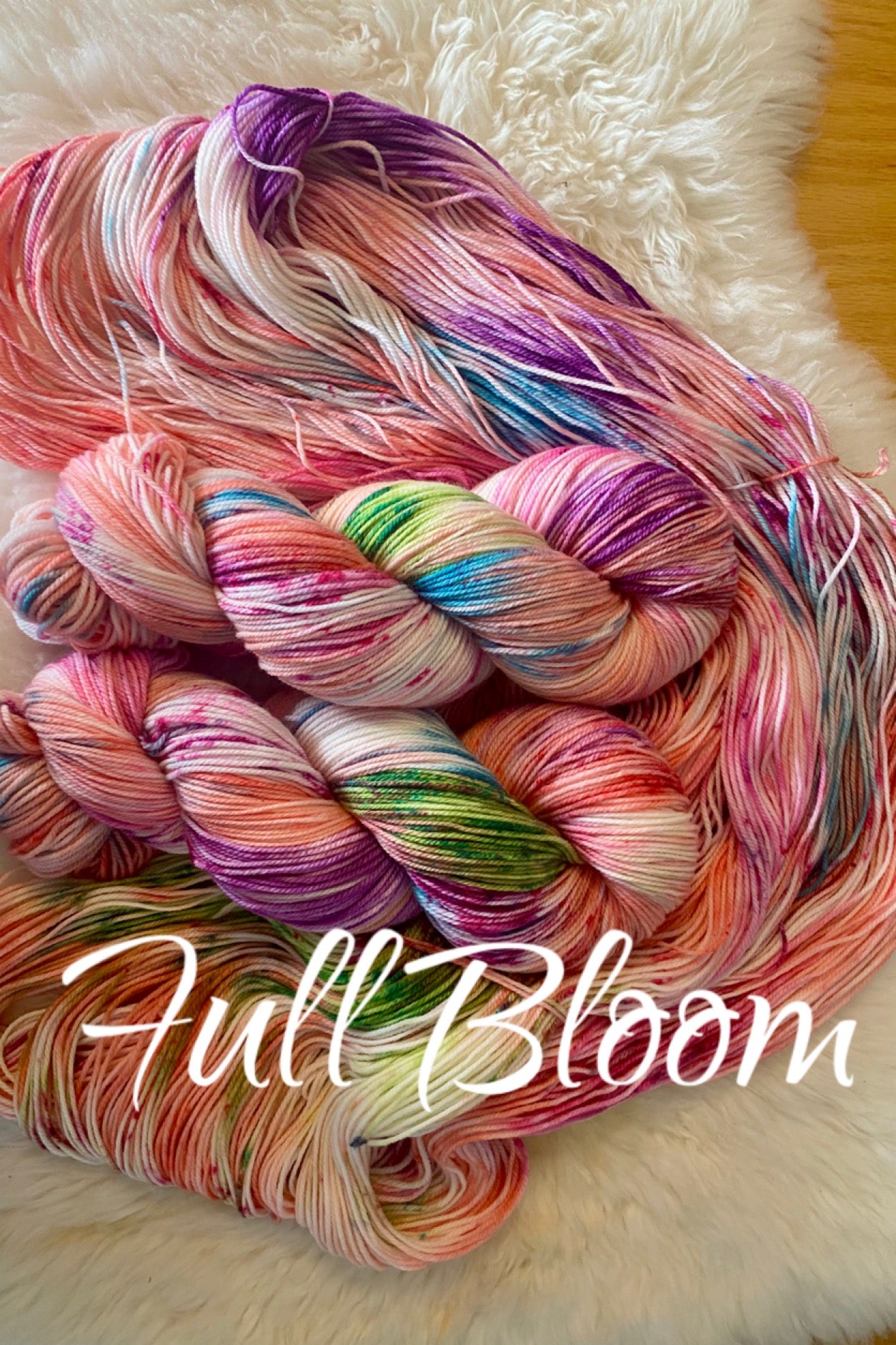 Multicolored yarn skein on a fluffy white surface with 'Full Bloom' text.